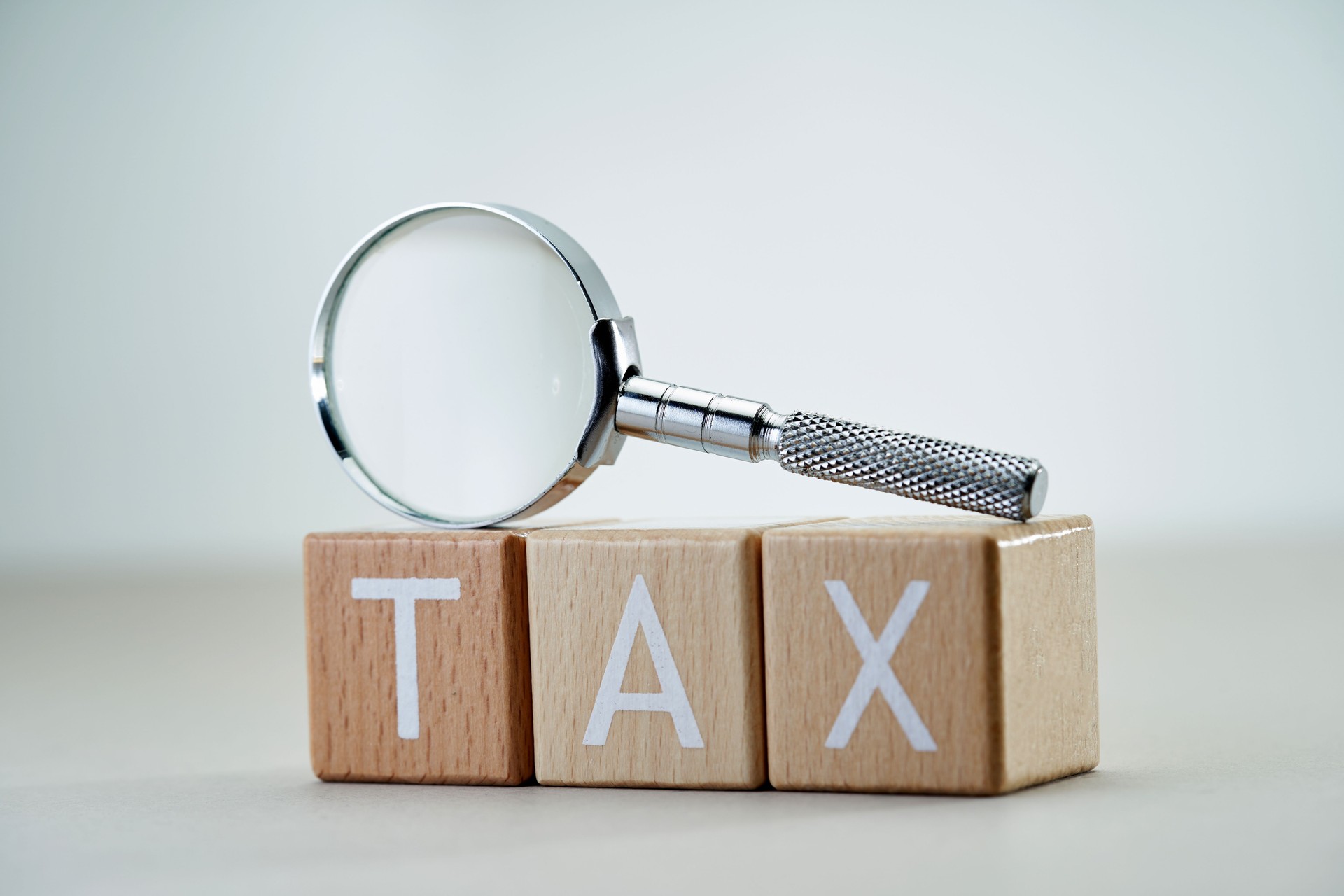 wooden blocks with single word tax and magnifying glass.